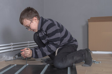 Caucasian boy 11 years old installs furniture in his room with a screwdriver