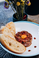 Beef steak tartare with raw egg yolk and croutons on a white plate. french cuisine. view from above