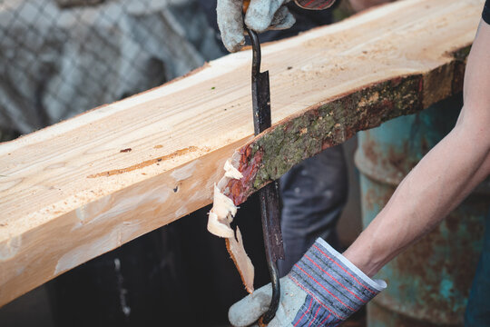 Handy woodcutter prepares larch wood for later processing. Planing wood. Working larch boards with traditional tools. Hand processing. Trimming the tree trunk