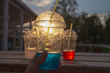 Carbonated water in plastic cups with cocktail tubes in the evening on a summer day in a street cafe