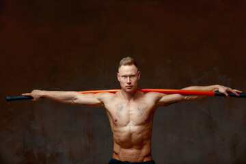 Obraz premium A fighter or karate man, stands in a fighting artificially pose and holds a bamboo stick on gray wall studio background.