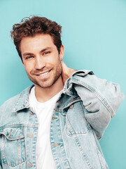 Portrait of handsome smiling stylish hipster lambersexual model with curly hairstyle. Sexy man dressed in jeans jacket. Fashion male isolated on blue wall in studio. Blue eyes