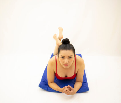 beautiful oriental athletic woman in gray sportswear and red blouse, exercising on her stomach with her neck stretched upwards on a blue mat, on a white background