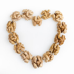 Frame of peeled walnuts flat layed in the shape of heart isolated on white background. Copy space. Top view.