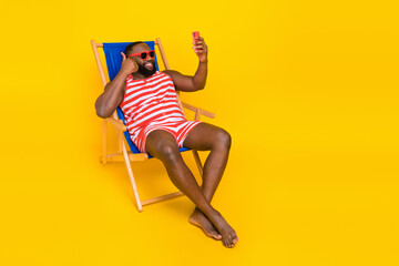 Guy tourist sit deckchair rest resort make selfie device thumb up sign wear suit swimsuit isolated shine color background