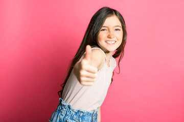 cute positive thumb up child over pink backgroud on studio