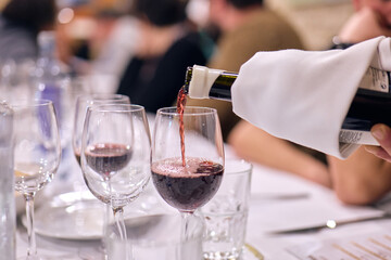 Hand of a waiter pouring red wine from a bottle into a glass