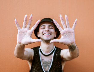 Young man with tattoos extending his arms while smiling and showing his long fingernails. Lgbti community and lifestyle.