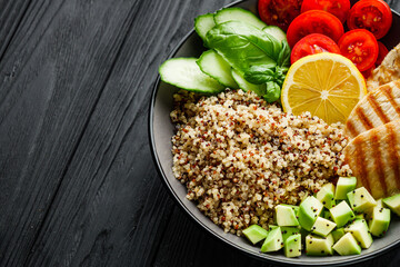 quinoa salad with grilled chicken and vegetables on a black wooden rustic background