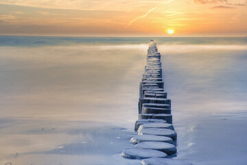 Groynes protruding into the horizon in the Baltic Sea. Long exposure with muted colors.