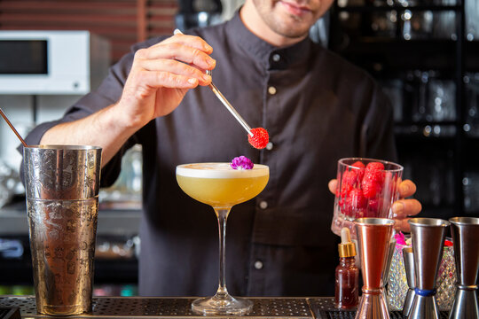 Crop anonymous barman decorating refreshing cocktail with raspberries