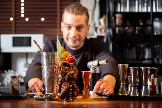Content young male bartender standing at counter with exotic tiki cocktail