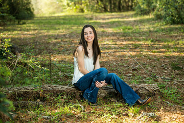 A beautiful happy teenage brunette girl sitting outdoors on a log hapy and smiling with copy space