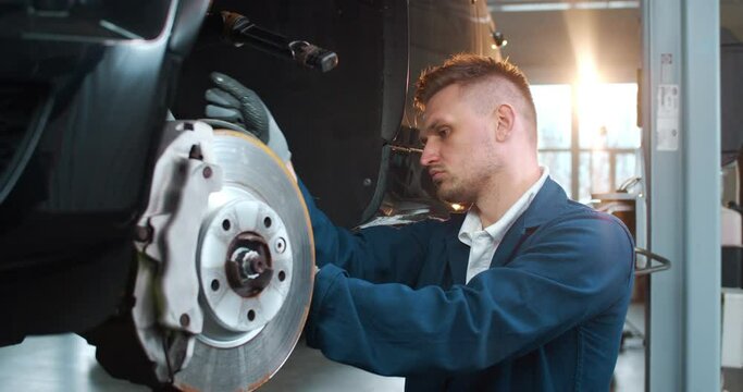 Caucasian young handsome man mechanic changing wheels in garage and working with wrench. Male worker of auto service change wheel with spanner. Repairing automobile conception. Workday of repairman.