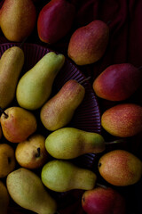 Yellow and red juicy fragrant pears lie on a cherry plate on a dark cherry tablecloth.