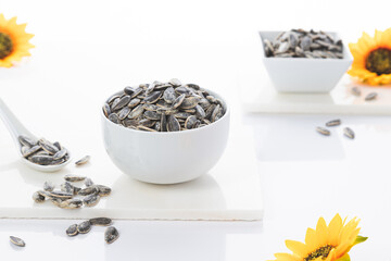 Two bowls of sunflower seeds with sunflowers on white  background. Selective focus.