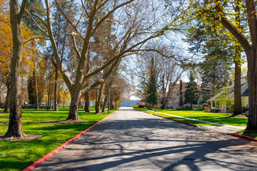 A shaded tree lined street of Victorian and historic homes across from the city park with the lake in view in historic Fort Grounds district of Coeur d'Alene, Idaho, USA.