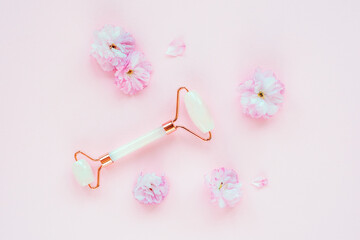 Face roller and sakura flowers on pink background. Skin care, beauty treatment concept. Top view, flat lay