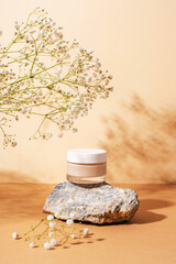 Cream in a jar on natural stone with gypsophila flowers in sunlight. Neutral beige background