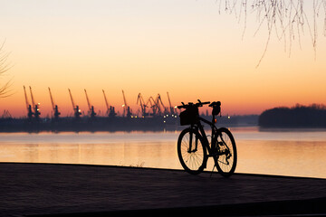 Fototapeta premium Silhouette of a bicycle against the backdrop of port cranes at dawn