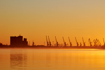 Orange sunrise over Danube river with silhouette of cranes in cargo port