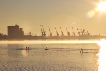 River landscape with silhouettes of people paddle on stand up paddle board (SUP) at sunrise on calm...