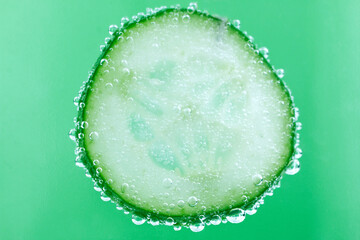 Cucumbers sliced in water with bubbles close up image on green background.