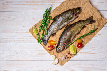 Raw fish, trout with on craft paper with ingredients for cooking. Fish, pepper, garlics, tomatoes, lemon and rosemary on white wooden table. Healthy food and dieting concept flat lay, top view image 