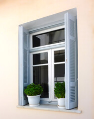 A simple white framed window with grey shutters and potted plants, Chora town, Andros island, Greece.