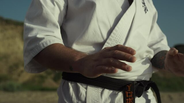 Black belt fighter training hands exercises practicing karate ion beach closeup.