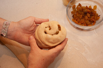 A baker rolls a braid of challah dough filled with raisins into a circle to create the traditional...