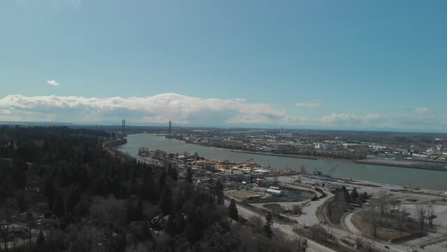 Scenic view of Delta BC on the edge of the Fraser river with the Alex Fraser bridge in the background Bright day blue sky clouds Aerial Wide reversing revealing neighbourhood next highway