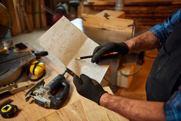 Close up of carpenter hands with blueprints plans to make a piece of furniture in the carpentry workshop