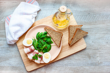 Plate with spinach leaves, green basil, bacon, eggs and a piece of rye bread. Olive oil. Healthy breakfast. Food for breakfast on wooden background. Flat lay