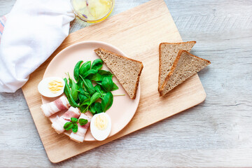 Plate with spinach leaves, green basil, bacon, eggs and a piece of rye bread. Olive oil. Healthy breakfast. Food for breakfast on wooden background. Flat lay