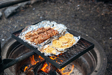 Pork kebab and onions are grilled on the foil over a campfire.