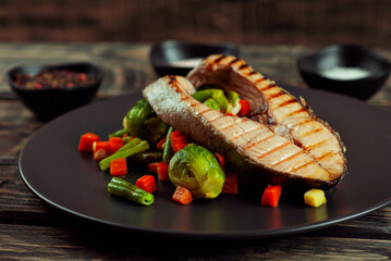 Grilled salmon steak. Red salmon with lemon and vegetables close up. wasps on a salad of boiled cabbage, carrots, green peas and broccoli. Food on shabby wooden table.