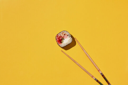 Fresh sushi roll and chopsticks on yellow background.