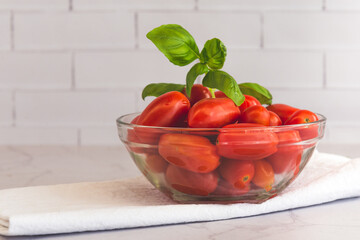 Tomates cherry frescos y albahaca en recipiente de vidrio transparente, sobre una mesada de...