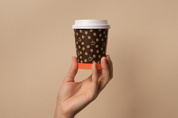 Mano femenina sosteniendo vaso de cafe desechable para llevar fondo marron