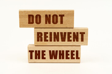 On a white surface are wooden blocks with the inscription - Do Not Reinvent The Wheel