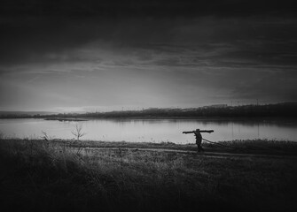 Person walking a country road carrying dry firewood. Peaceful sunset, black and white scene and wanderer silhouette on trail. Idyllic and moody rural landscape