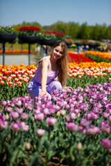 A young woman in a pink suit stands in a blooming field of tulips. Spring time