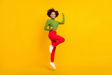 Full size profile side photo of young excited girl jump up rejoice luck fists hands triumph isolated over yellow color background