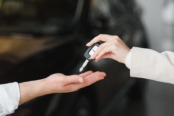 Car sale. Dealer giving key to new owner in auto show or salon, closeup