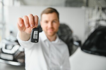 Happy buyer holding keys near the car in front of the modern avtosalon building