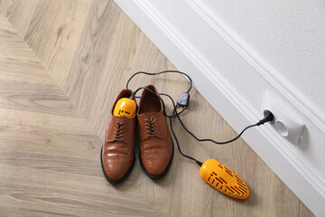 Pair of stylish shoes with modern electric footwear dryer on floor indoors, above view