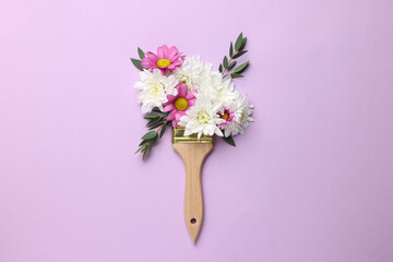 Brush with colorful flowers of chrysanthemum on violet background, top view. Creative concept