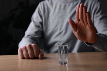 Obraz na płótnie Canvas Man refusing to drink vodka at wooden table, closeup. Alcohol addiction