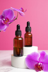 Fototapeta na wymiar Beauty collagen face oil in a glass dropper bottles on podium with orchid flowers. Trendy shoot of cosmetics packaging. Essential oil with natural ingredients.